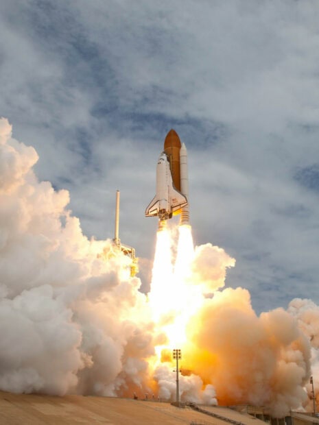 A space shuttle lifting off with fiery engines and thick smoke clouds at launch site
