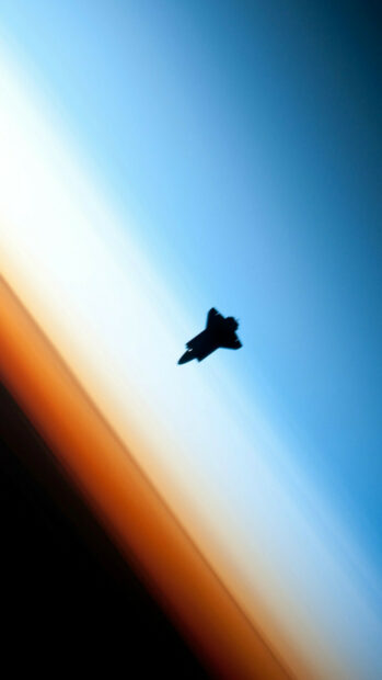 Space shuttle flying above the Earth's horizon during sunset in space