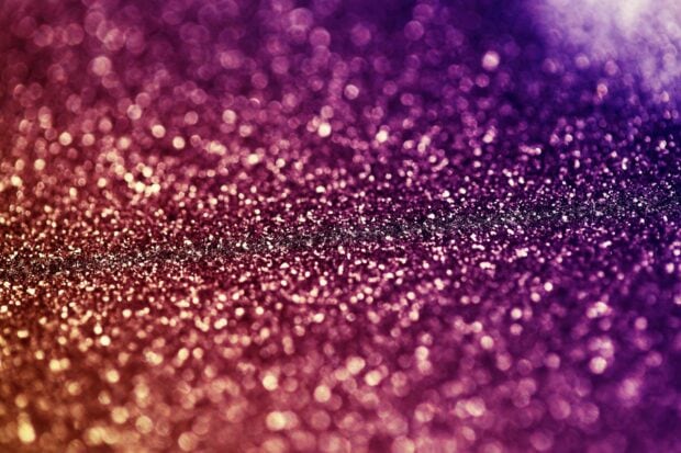 Close up of sparkle texture with glitter and bright shining particles in purple and gold tones