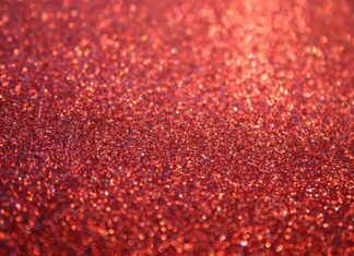 A close up of sparkle texture with shiny red glitter particles scattered evenly across the surface