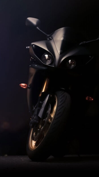 Close up of sports bike front wheel and headlight in dark setting with golden rims