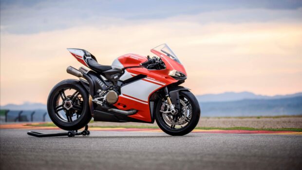 A red and white sports bike parked on the racetrack with a scenic mountain background