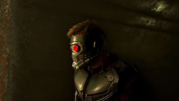 Star Lord wearing his helmet with a glowing red eye in a dark environment