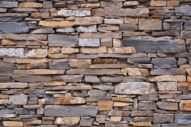 A close up view of a stone wall with various shapes and shades of stones stacked tightly together