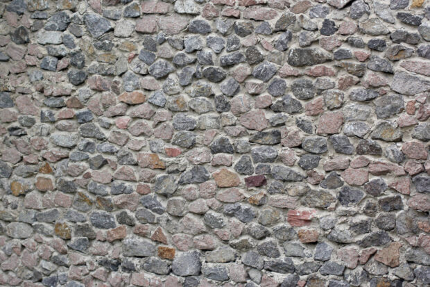 A close up view of rough textured stone wall with various colored stones arranged tightly together