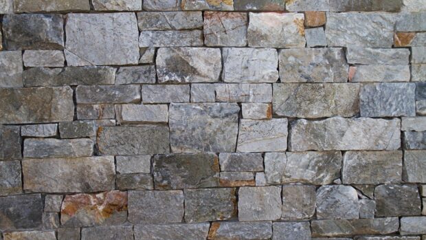 A close up view of a stone wall showing various textured stone blocks arranged neatly