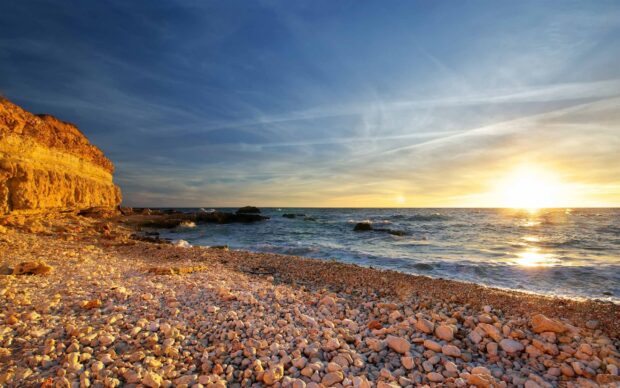 Golden cliffs and stone beach under a clear sky at sunset with ocean waves