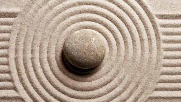 A single stone surrounded by concentric circles in fine sand forming a Zen stone pattern