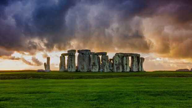 Ancient stone structure standing on green grass under dramatic cloudy sky