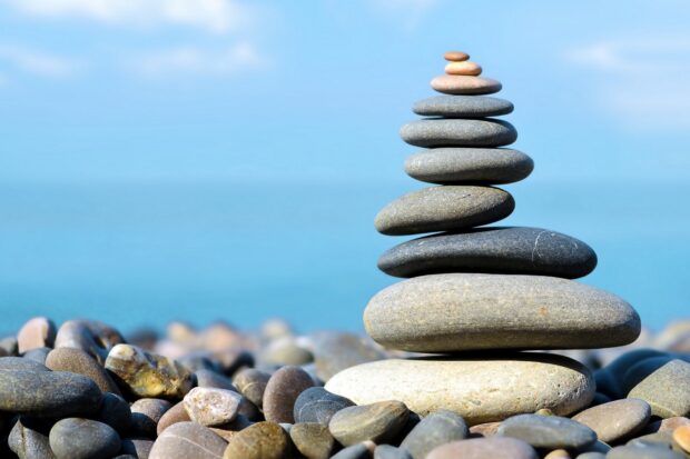 A stack of smooth natural stones balanced on a pebble beach near calm blue water