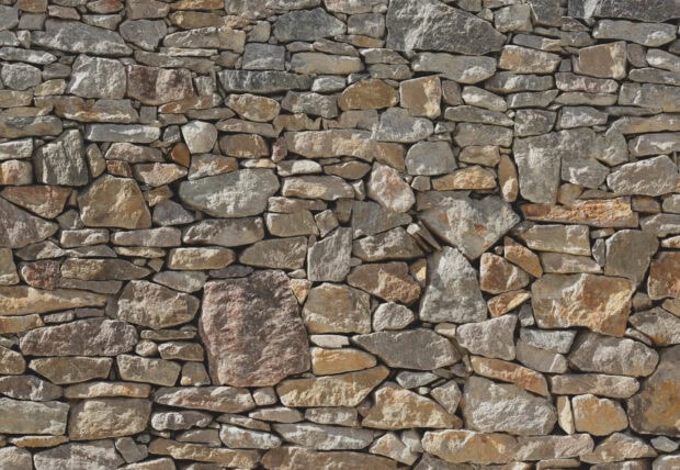 A close up view of a textured stone wall with various shapes and colors of stone bricks
