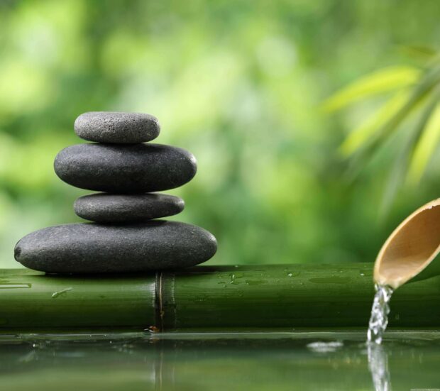 Balanced stack of stones on bamboo with flowing water in a zen garden setting