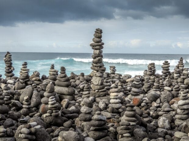 Balanced stone stacks at rocky ocean shore under cloudy sky