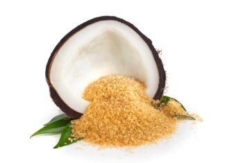 Brown sugar granules spilling from a halved coconut shell on green leaves