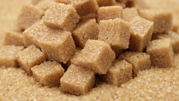 Brown sugar cubes neatly stacked on a pile of granulated sugar crystals