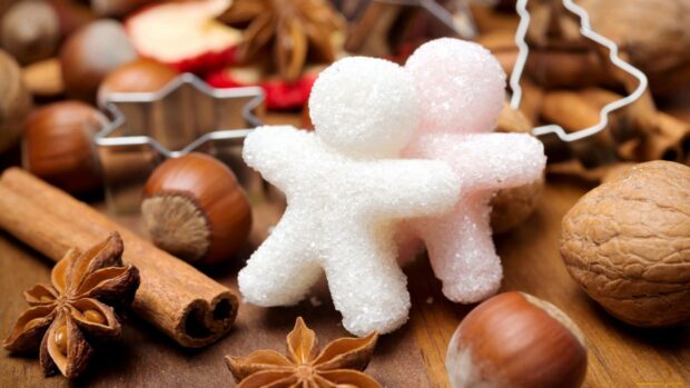 White and pink sugar figures shaped like gingerbread men surrounded by cinnamon and nuts