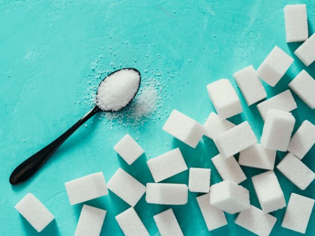 White sugar cubes and granulated sugar on a black spoon on a blue surface