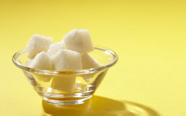 White sugar cubes placed in a clear glass bowl on a yellow surface