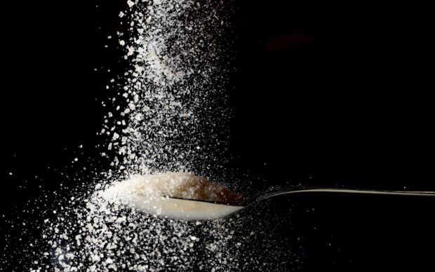 White sugar granules falling into a spoon with sugar crystals around on a black background