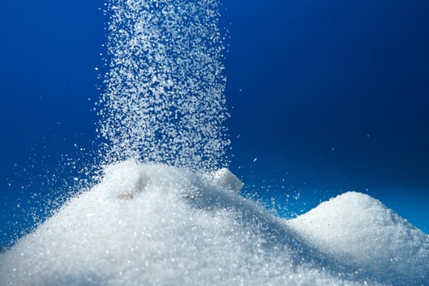 White sugar granules falling on a pile of sugar crystals against a blue background