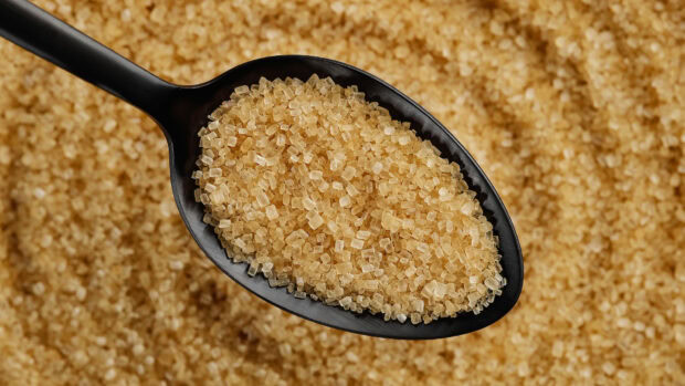 Close up of raw sugar crystals on a black spoon with a pile of sugar grains