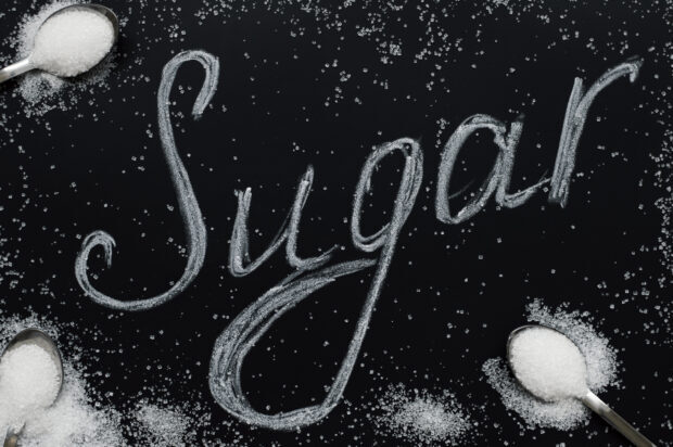 Granulated sugar spelled out on black surface with spoons of sugar scattered around