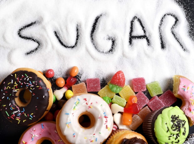 The word sugar written in white sugar with colorful donuts and candies below on a black surface
