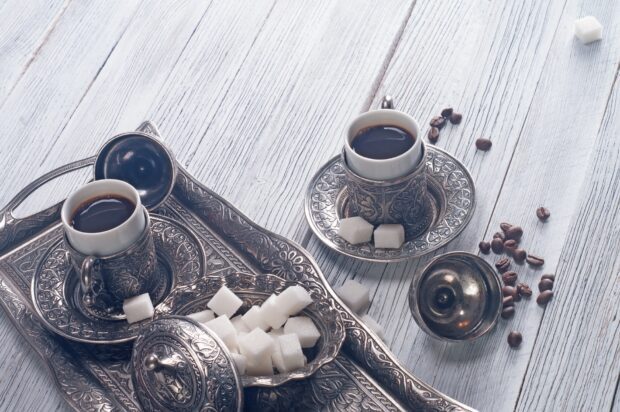 Two cups of coffee with sugar cubes on an ornate tray on a wooden table