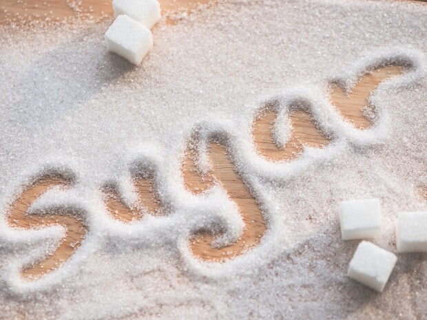 The word sugar written in granulated sugar on a wooden surface with sugar cubes nearby