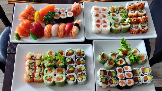 A variety of sushi rolls and sashimi featuring salmon and avocado on white plates
