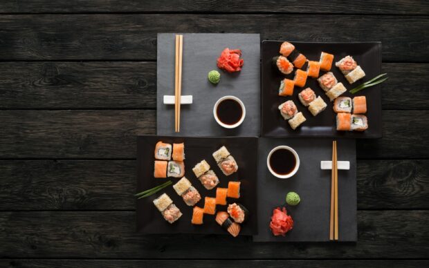 A variety of sushi rolls arranged on black plates with chopsticks ginger wasabi and soy sauce on a dark wooden table