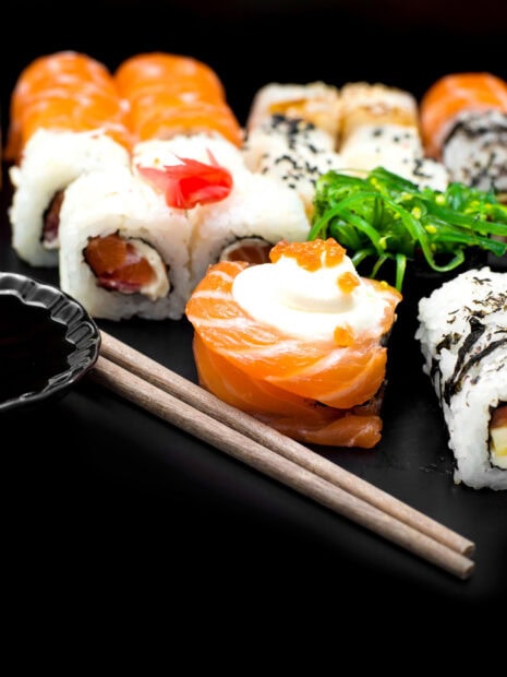 A variety of sushi rolls with fresh salmon and seaweed salad on a black plate with chopsticks