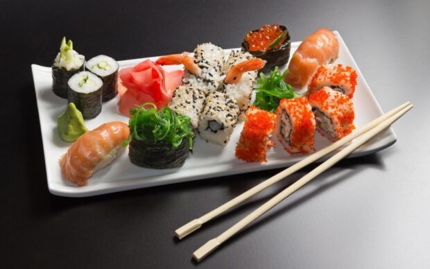 A variety of sushi rolls with seaweed salad and ginger on a white plate
