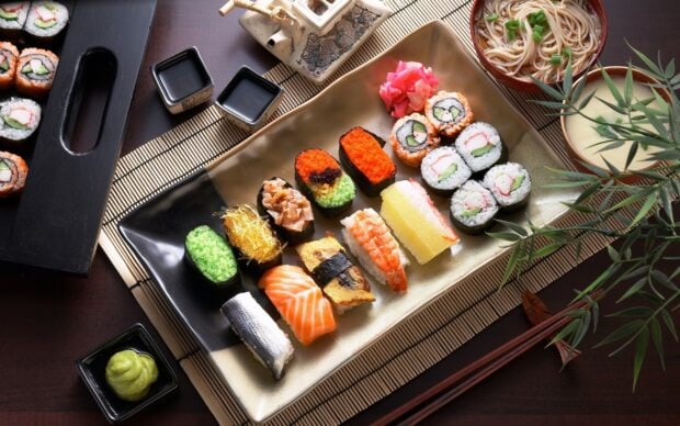 Assorted sushi rolls and nigiri with chopsticks and dipping sauces on a table setting
