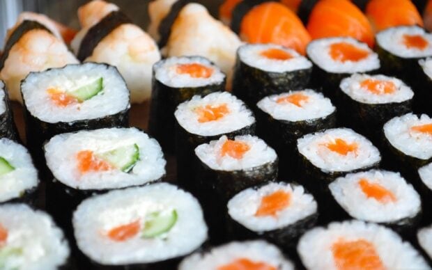 Close up of sushi rolls with cucumber and salmon in a wooden tray