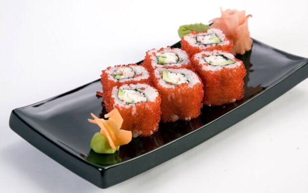 Sushi rolls with tobiko and cucumber served on a black rectangular plate with wasabi and pickled ginger