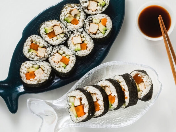 Sushi rolls with tofu and vegetables arranged on fish shaped plates with soy sauce and chopsticks