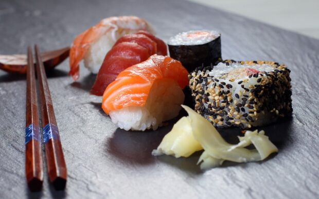 A close up view of sushi pieces arranged with chopsticks and pickled ginger on a dark plate