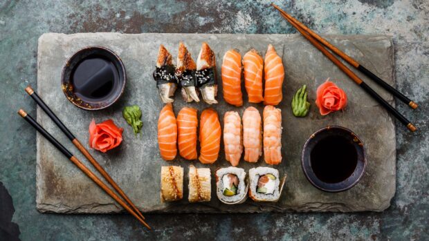 An assortment of fresh sushi arranged on a stone platter with chopsticks and soy sauce