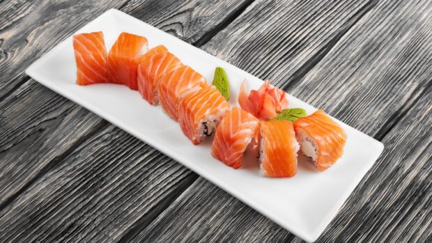 Fresh salmon sushi pieces served on a white plate with garnishes on a wooden table