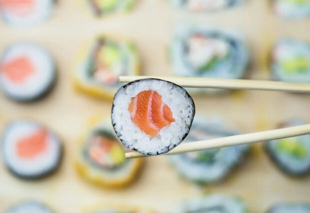Fresh salmon sushi held by chopsticks with blurred sushi background
