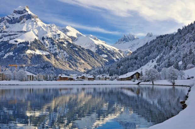 Snowy Swiss village reflected in a lake with snowy mountains in Switzerland wallpaper