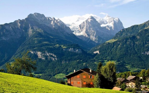 A scenic view of Swiss mountain landscape with green fields and traditional wooden houses