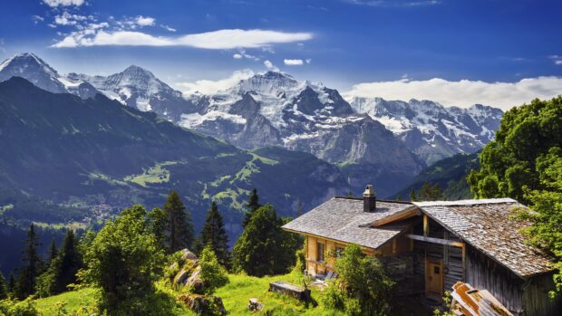Traditional Swiss cabin surrounded by lush greenery and snow capped mountains in Switzerland