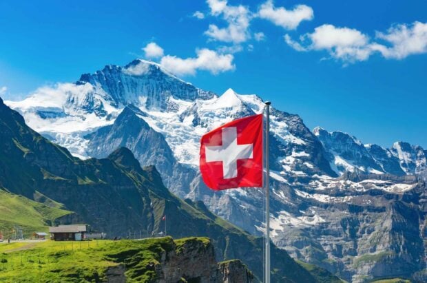 Swiss flag waving in front of snowy mountains in Switzerland landscape