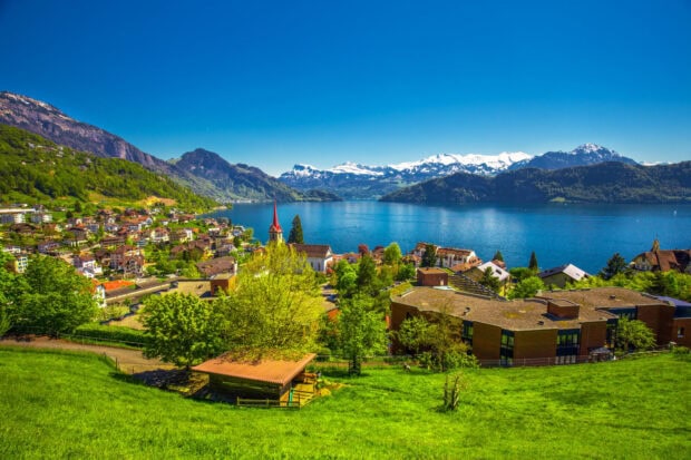 A scenic Switzerland village with green hills and snowy mountains by the blue lake