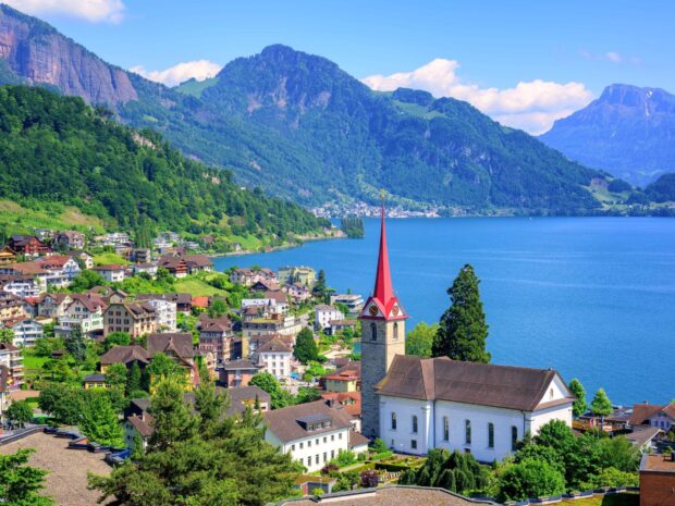 A charming Switzerland village with a red steeple church near a blue lake and green mountains