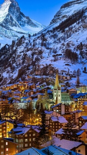 Snowy village landscape in Switzerland with mountains and clock tower at dusk