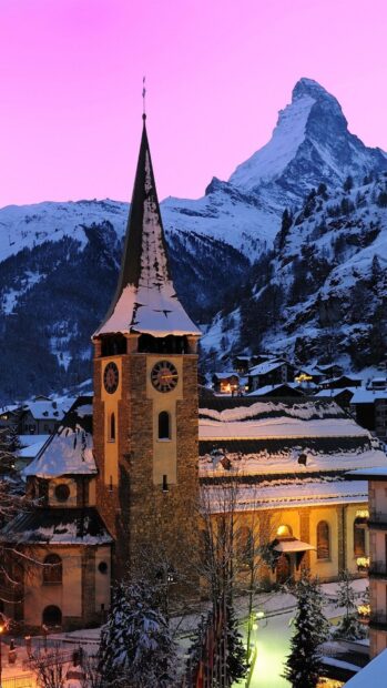 Snowy church tower in Switzerland with mountain peaks at sunset