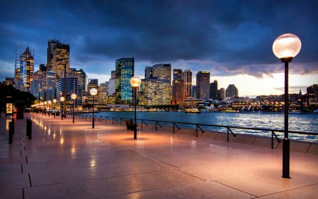 Evening view of Sydney city skyline with illuminated waterfront street lamps and harbor